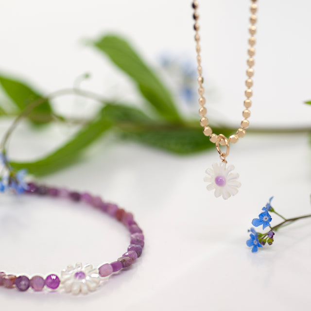 Necklace with a flower pendant on a white background with green leaves and flowers.