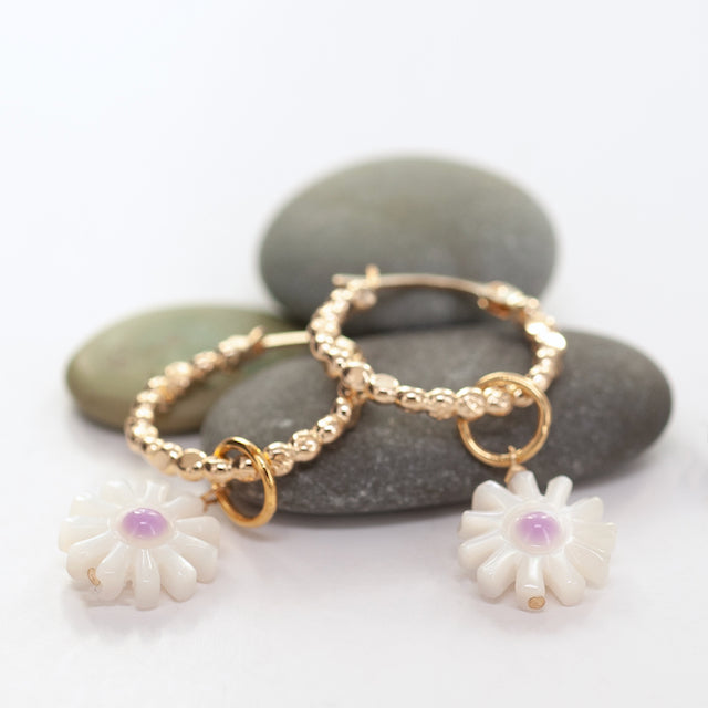 Gold hoop earrings with white flower charms on a white background