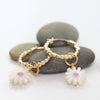 Gold hoop earrings with white flower charms on a white background